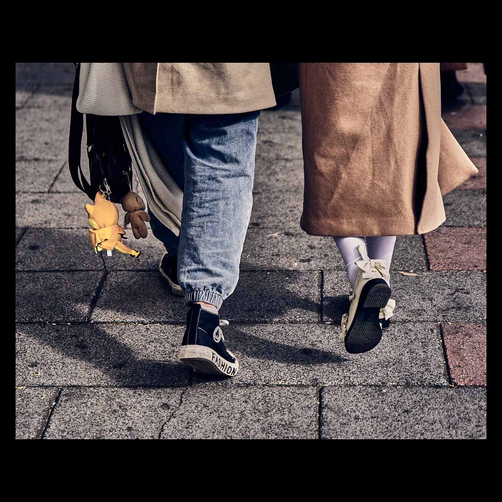 Escena de calle de los pies de una pareja andando con un calzado llamativo donde dice 