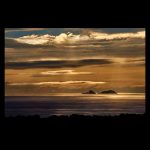 Puesta de sol que se refleja sobre el mar y las nubes dejan pasar los últimos rayos de la hora dorada