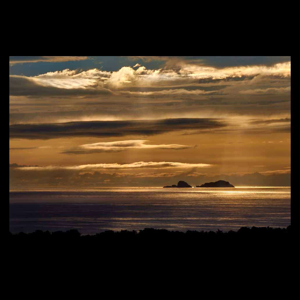 Puesta de sol que se refleja sobre el mar y las nubes dejan pasar los últimos rayos de la hora dorada