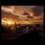 Jinetes cabalgando envueltos por la luz dorada del atardecer