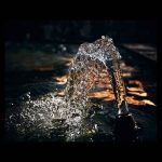 Chorro de agua congelado en alta velocidad con texturas de cristal y reflejos dorados sobre un fondo negro absoluto, fotografía artística de alta resolución.
