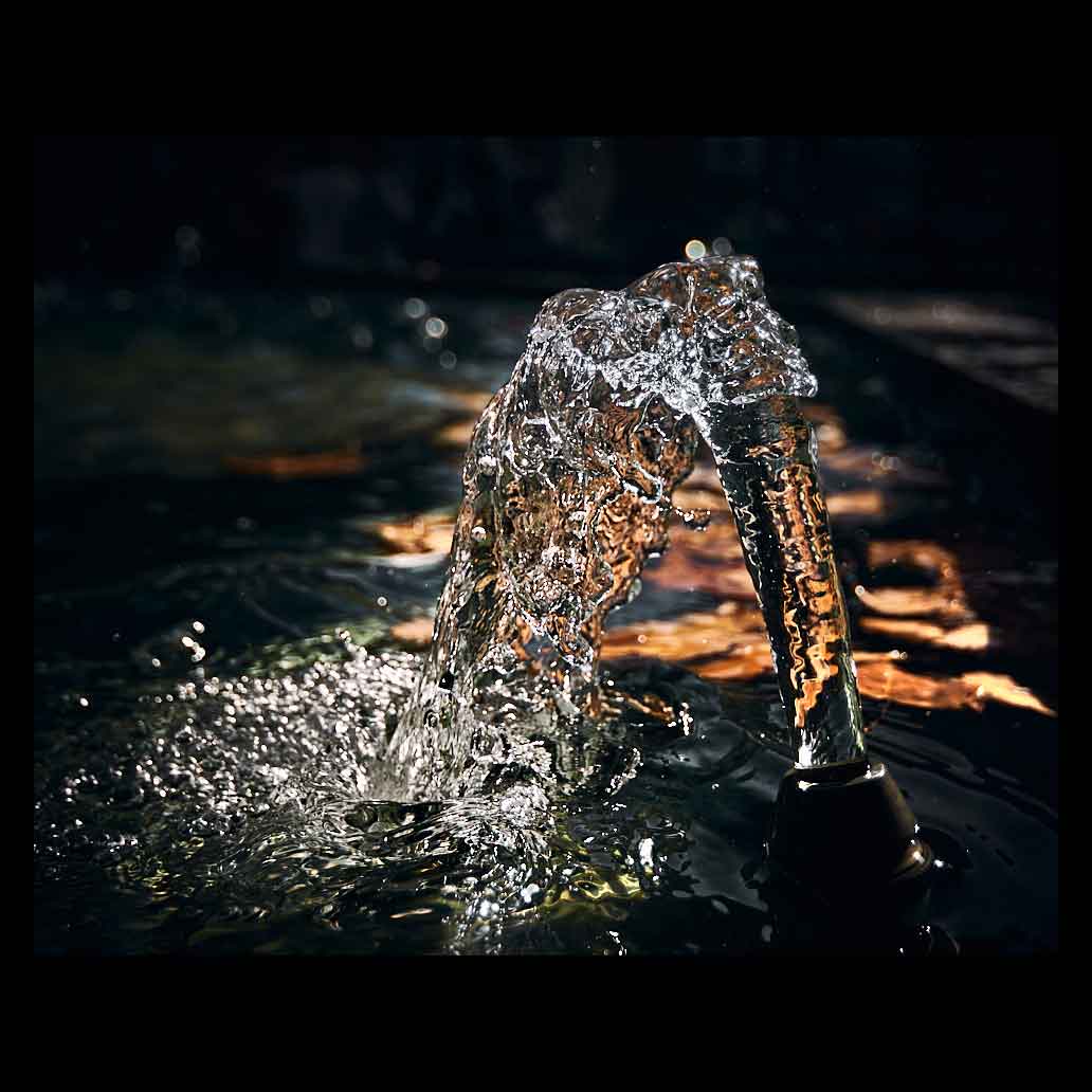 Chorro de agua congelado en alta velocidad con texturas de cristal y reflejos dorados sobre un fondo negro absoluto, fotografía artística de alta resolución.